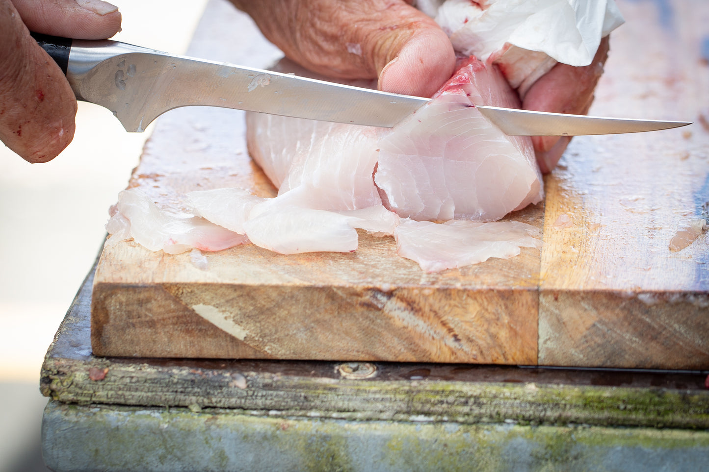Person cutting fish fillets on a wooden cutting board with a knife.
