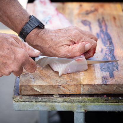 Person cutting fish on a wooden cutting board with a knife.